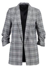 Long blazer à carreaux gris avec manches retroussées et doublure intérieure noire, coupe ajustée sans boutons.