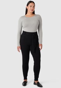 Šedé tričko s dlouhým rukávem v kombinaci s černými kalhotami s vysokým pasem a detaily vázání v pase. Hladký materiál, úzký střih a elastická tkanina.