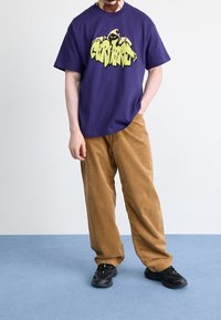 Lilla bomuld t-shirt med grafisk tryk; brune manchesterbukser; sorte sportssko. Enkel, afslappet pasform; ingen synlige mønstre på bukserne.