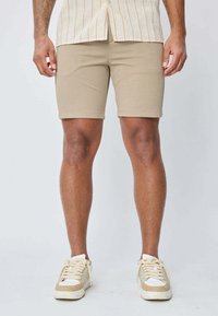 Shorts kaki en mélange de coton extensible, avec une coupe ajustée. Assortis à des baskets de couleur claire. Apparence simple et homogène.