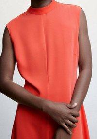 Rotes ärmelloses Kleid mit hohem Ausschnitt, das eine klare Silhouette, eine Vordernaht und eine glatte Stofftextur aufweist. Keine sichtbaren Muster oder Akzente.