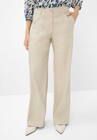 Pantaloni beige a gamba larga realizzati in tessuto leggero, con tasche anteriori e una texture liscia, abbinati a scarpe bianche con punta.