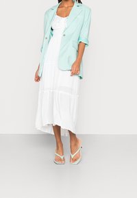 Miętowy blezer noszony na białej, teksturowanej sukience midi z falbaniastymi warstwami; w zestawie z miętowymi sandałami. Czyste linie i jasne kolory.