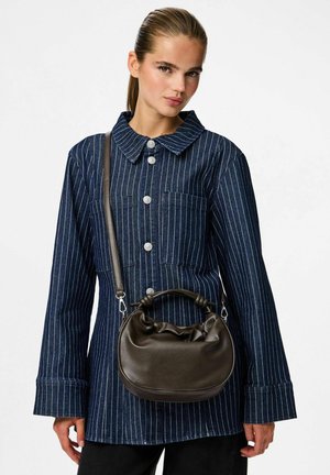 Donna che indossa una giacca a righe blu navy con grandi bottoni, mentre porta una piccola borsa in pelle marrone scuro con manico annodato e tracolla.