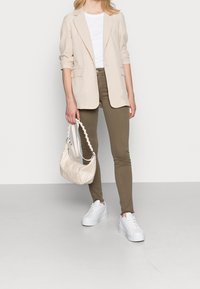 Blazer a cuadros beige y blanco, camiseta blanca, vaqueros skinny verde oliva, bolso crema con asa texturizada y zapatillas blancas con plataforma.