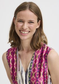 Värikäs ilmanhiha toppi, jossa on geometrinen kuvio pinkissä, purppurassa ja keltaisessa väriskaalassa, sileällä pinnalla ja V-mallin kaula-aukolla.
