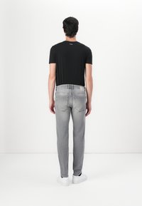 Svart t-skjorte med korte ermer kombinert med lysegrå jeans og hvite sneakers, vist fra baksiden. Har et glatt stoff og minimalistisk design.
