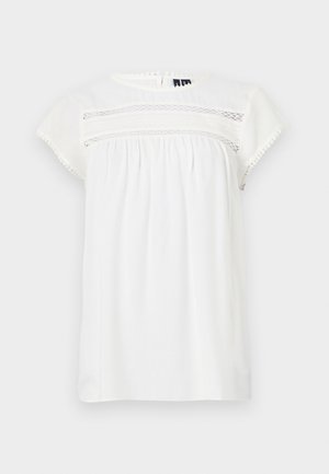 Vit kortärmad blus med rund hals, samlad design och dekorativ spetsdetalj fram, med en scallopad nederkant.