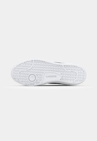 Semelle de sneaker noir et blanc avec un motif de texture antidérapante, présentant un élément de design circulaire et la marque "Lacoste" embossée sur le côté.