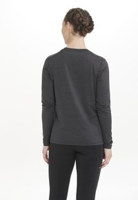 Langärmliges Shirt in Dunkelgrau, aus strukturiertem Stoff, mit einem runden Halsausschnitt und taillierter Passform, kombiniert mit schwarzen Leggings.