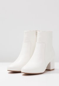 Botas de tobillo blancas fabricadas en material suave, con tacón cuadrado, puntera redondeada y cremallera lateral. Diseño minimalista sin patrones ni acentos.