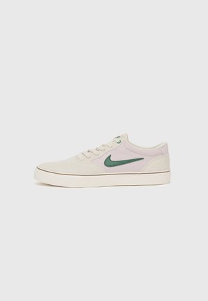 Beige Wildlederturnschuhe mit grünem Leder-Nike-Swoosh, weißer Gummisohle, runder Zehenpartie und Schnürverschluss. Minimalistisches Design mit angenehm weicher Textur.