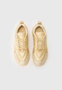 Beige joggesko med teksturert syntetisk overdel, polstret såle og snørelukking. Har en logo på tungen og hæltappen.