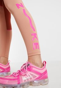 Legginsy Nike w odcieniu nude z jasnoróżowym logo oraz dopasowanymi różowymi butami Nike z przezroczystą podeszwą i przewiewnym materiałem.