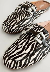 Schwarz-weiße Zebra-Print-Pantoletten aus glattem Haar-Haut. Mit einem braunen Lederband und silberfarbenen Metallakzenten.