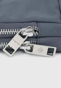 Pochette en tissu gris dotée d'une double fermeture éclair avec des tirettes en métal argenté, incluant le logo et une texture non ornée.