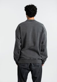 Sudadera gris carbón con un corte relajado, cuello redondeado y costuras de hombro caídas, combinada con jeans de mezclilla oscura.