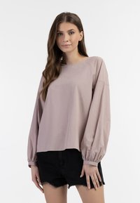 Lys lyserød bluse med lange ballonærmer, rund halsudskæring og en afslappet pasform, parret med sorte slidte denimshorts.