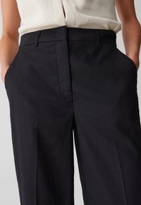 Pantalons noirs sur mesure avec une coupe droite, dotés de poches latérales et d'une texture lisse, fabriqués à partir d'un tissu léger.