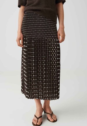 Femme portant une jupe midi plissée noire à pois blancs, un pull marron à manches courtes et des sandales marron à talons.