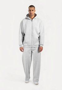 Sudadera con capucha gris con cremallera y bolsillos frontales, combinada con pantalones deportivos grises a juego. Confeccionada con tela suave y texturizada. Diseño minimalista.