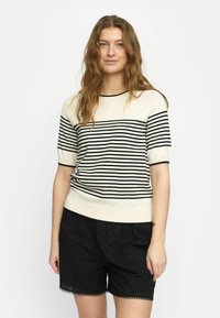 Cremfarbener und schwarzer, gestreifter Strickpullover mit kurzen Ärmeln und geripptem Saum, kombiniert mit schwarzen, strukturierten Shorts mit gewelltem Saum.