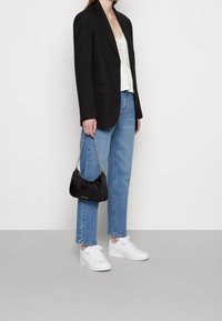 Blazer noir, haut blanc, jean bleu clair et baskets blanches. Sac à épaule noir avec chaîne en argent. Silhouettes simples et contemporaines.