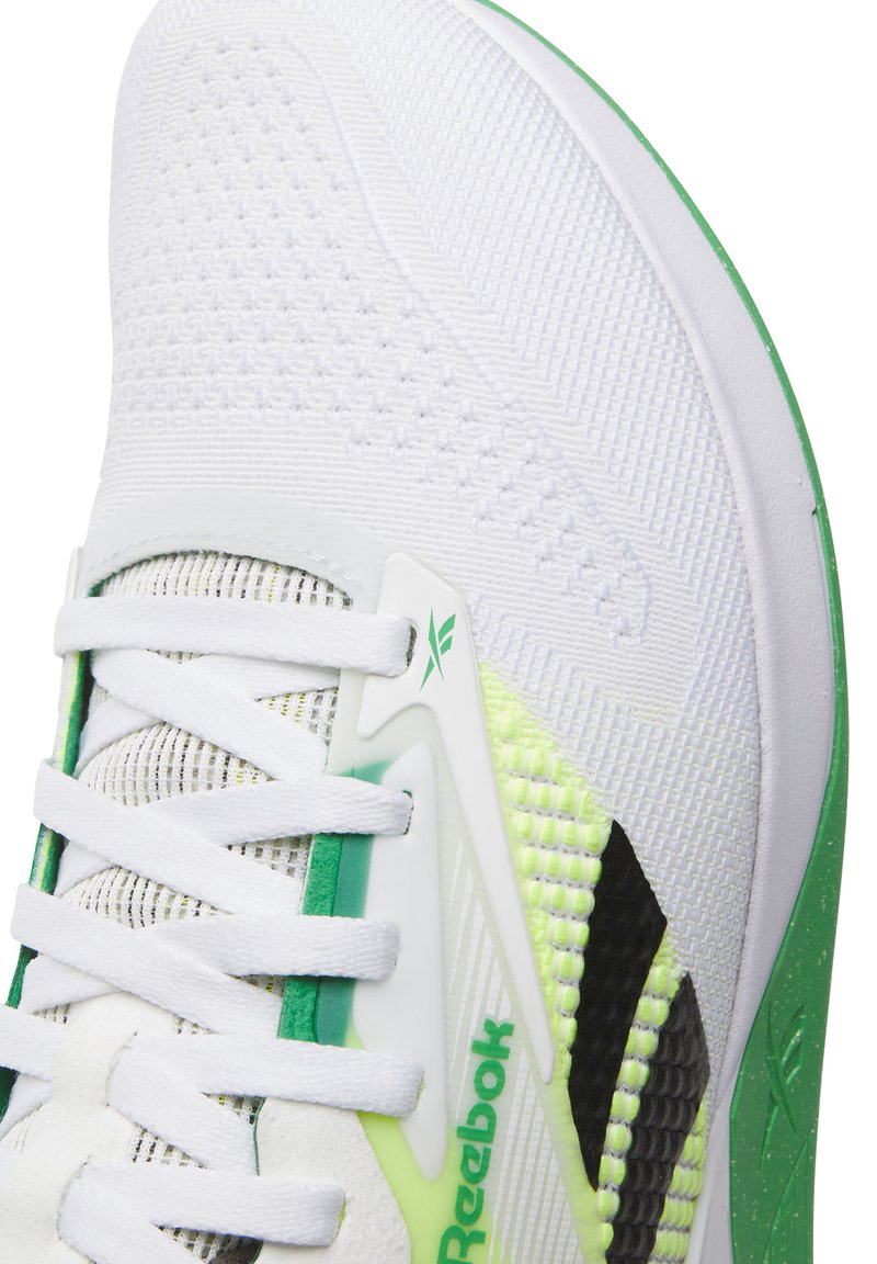 Zapatilla deportiva blanca con tejido de malla, acentos verdes y suela texturada. Incluye cordones blancos y un logo de Reebok en verde.