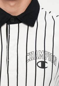 Polo tričko s černobílými pruhy, černým límečkem, knoflíkovým zapínáním a výrazným logem "Champion" na přední straně.