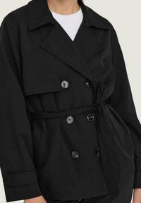 Veste noire à double boutonnage en tissu doux. Dotée de gros boutons et d'un détail de taille nouée. Col cranté et coupe décontractée avec manches longues.