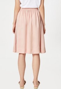 Nainen, jolla on polvimittainen vaaleanpunainen hame, jossa on joustava vyötärö, yhdistetty valkoiseen toppiin ja avonaisiin sandaaleihin.