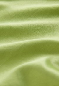 Tissu vert clair avec une texture lisse et brillante et des plis subtils, présentant un éclat doux sur la surface textile.