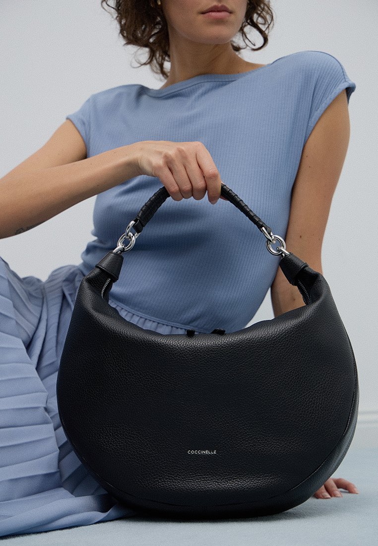 Borsa a mano in pelle nera con forma arrotondata, superficie testurizzata, manico intrecciato e dettagli in metallo argentato. Nome del marchio visibile sul davanti.