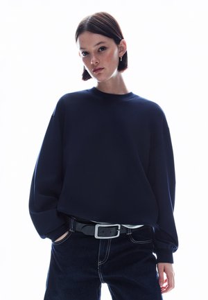 Navy blue oversized sweatshirt with a round neckline and dropped shoulders, paired with dark jeans and a silver-buckled black belt.