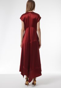 Langs rood satijnen jurk met korte mouwen, asymmetrische zoom en een sleutelgatdetail op de rug. Gladde textuur en elegante val.