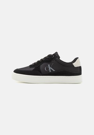 Czarny sneaker z połączeniem gładkiej i zamszowej tekstury, biała gumowa podeszwa i wyraźne srebrne logo po boku.
