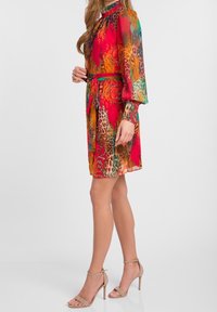 Korta ärmar röd klänning med djurmotiv och livfulla färger, åtdragen i midjan med ett matchande bälte; har en hög halsringning.