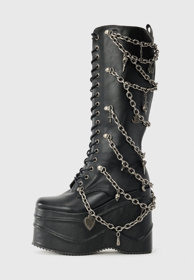 Melnas platforma kaujas zābakus ar sudraba ķēdes detalizāciju, kas ietver dekoratīvas piekariņas. Materiāls ir gluda āda, ar augstu un masīvu papēdi.