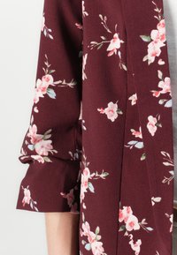 Kimono floreale marezza in tessuto testurizzato, con motivi di fiori rosa pastello e verdi, e maniche arrotolate.