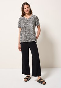 Top a maniche corte a strisce zebra in bianco e nero con scollo a V, abbinato a pantaloni neri larghi e sandali neri con fibbia dorata.
