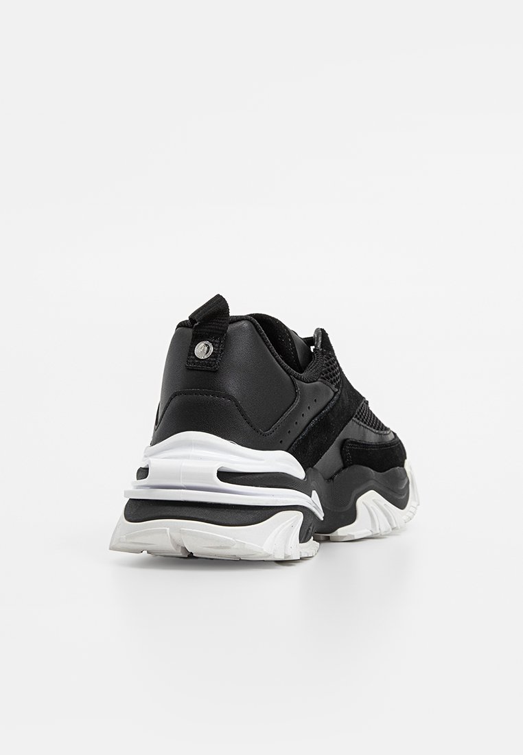 Baskets de sport noires avec un upper en maille texturée, des accents en cuir lisse, une semelle blanche épaisse et une languette au talon.