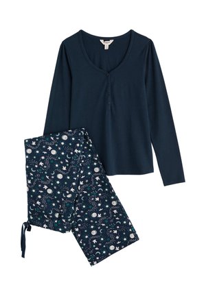 Granatowa bluzka z długim rękawem z detalem w postaci guzików, w połączeniu ze wzorzystymi spodniami z motywami księżyców, gwiazd i kwiatów w kolorze białym i teal.