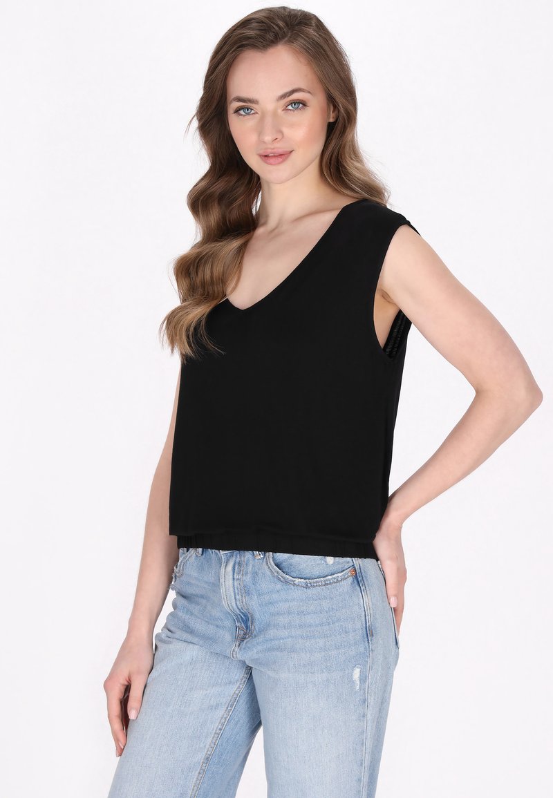 Sort ærmeløs crop top med V-halsdesign, lavet af blødt stof. Kombineret med lyseblå slidte denimjeans.