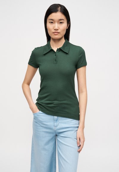 Πράσινο ριγωτό πόλο μπλουζάκι με γιακά και κοντά μανίκια. Το ύφασμα φαίνεται ελαστικό. Συνδυάζεται με ανοιχτό μπλε παντελόνι καμπάνα.