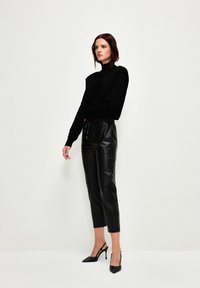 Zwarte gebreide coltrui gecombineerd met zwarte faux leren broek. Slank ontwerp met cropped lengte en trekkoord in de taille. Hoge hakken.