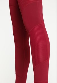 Czerwone legginsy sportowe z dopasowanym krojem. Teksturowane akcenty paneli i gładki materiał tworzą smukłą sylwetkę z widocznymi detalami szwów.