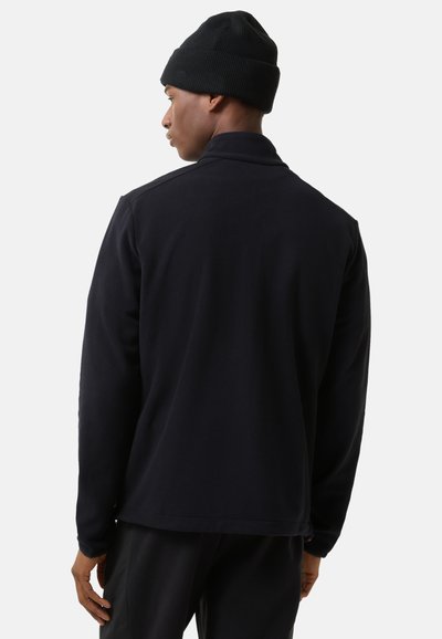 Black fleece jacket with a collar, long sleeves, and a relaxed fit. Worn with a black knit beanie. Minimalist design, no visible patterns.