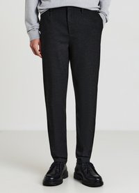 Dunkelgraue, maßgeschneiderte Hose mit glatter Textur, mit geradem Bein und dezenten vorderen Falten. Kombiniert mit schwarzen Schuhen.