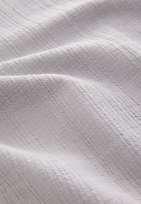 Tessuto grigio chiaro con trama testurizzata e un motivo superficiale sottile e irregolare, che mostra pieghe morbide e una caduta naturale.