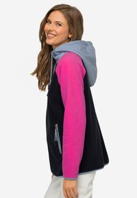 Giacca in pile di colore blu navy con maniche rosa e cappuccio azzurro chiaro. Presenta una tasca con zip e dettagli della zip a contrasto.